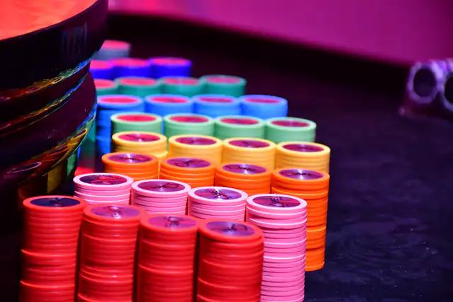 Stacks of red, pink, orange, green and blue casino chips glowing under magenta table lights