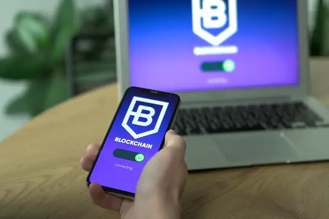 Hand holding a smartphone in front of a laptop with an app loading
