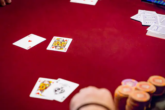 Ace of hearts and queen of diamonds face up on red felt beside a player's chip stack